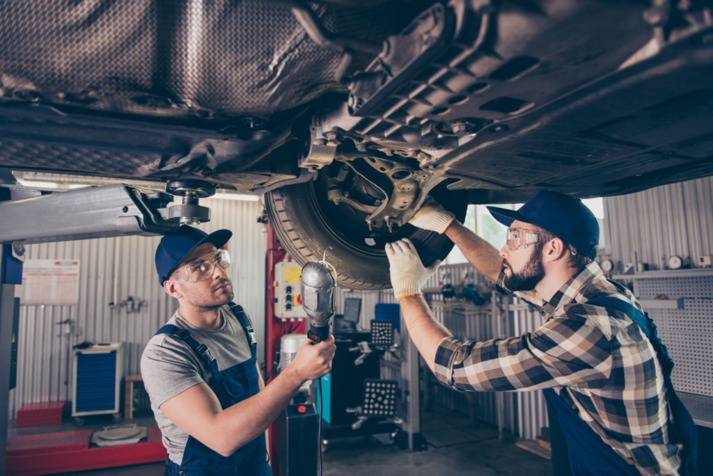 Two auto technicians working under a lifted vehicle, inspecting and repairing the suspension.