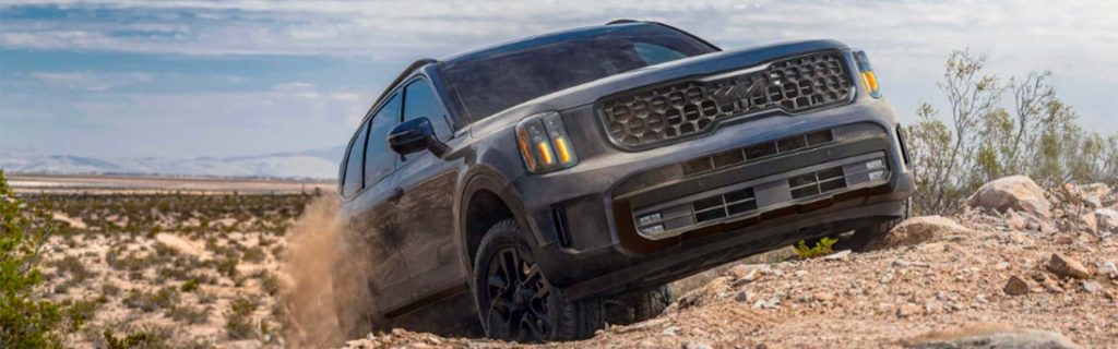 Kia Telluride SUV driving off-road through rocky desert terrain.